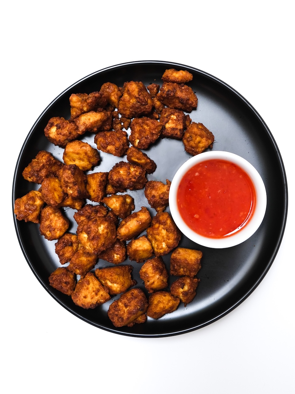 fried tofu on a black plate with red dipping sauce
