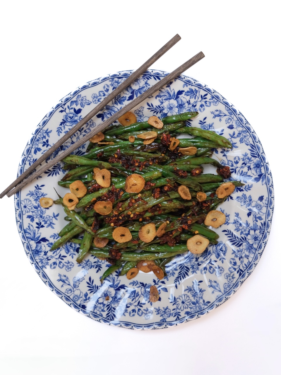 green beans topped with chili crisp and fried garlic chips on a blue patterned plate