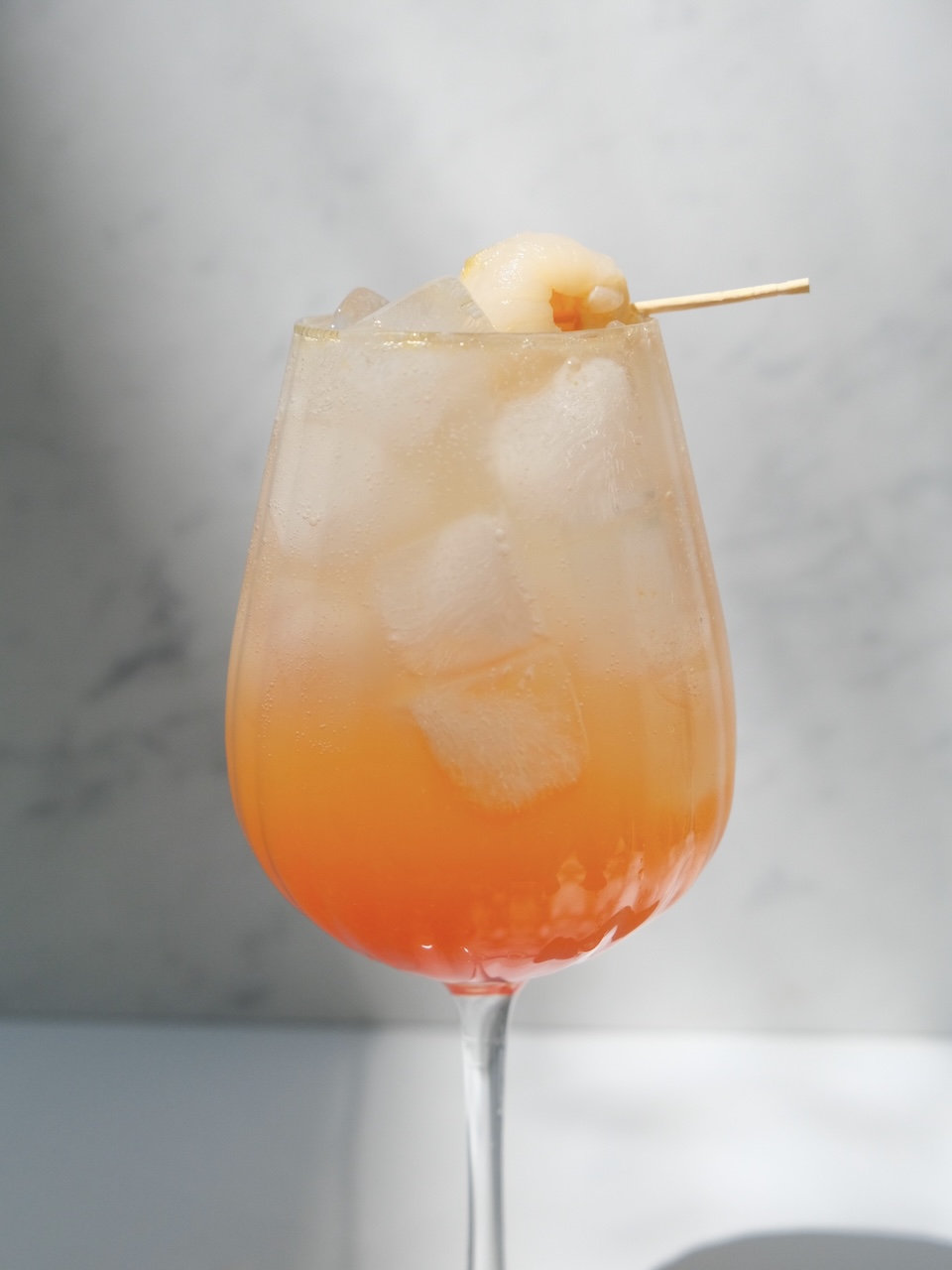 orange sunrise cocktail in a wine glass garnished with lychee