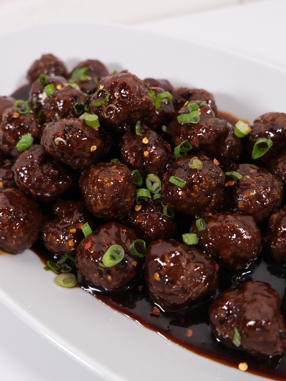 saucy meatballs garnished with scallions on a white plate