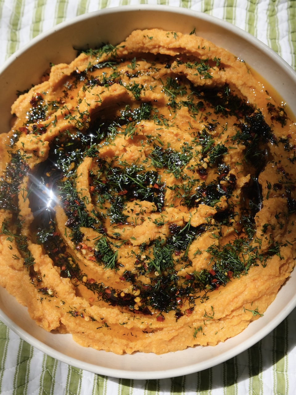 orange carrot dip topped with dill oil in a beige shallow bowl