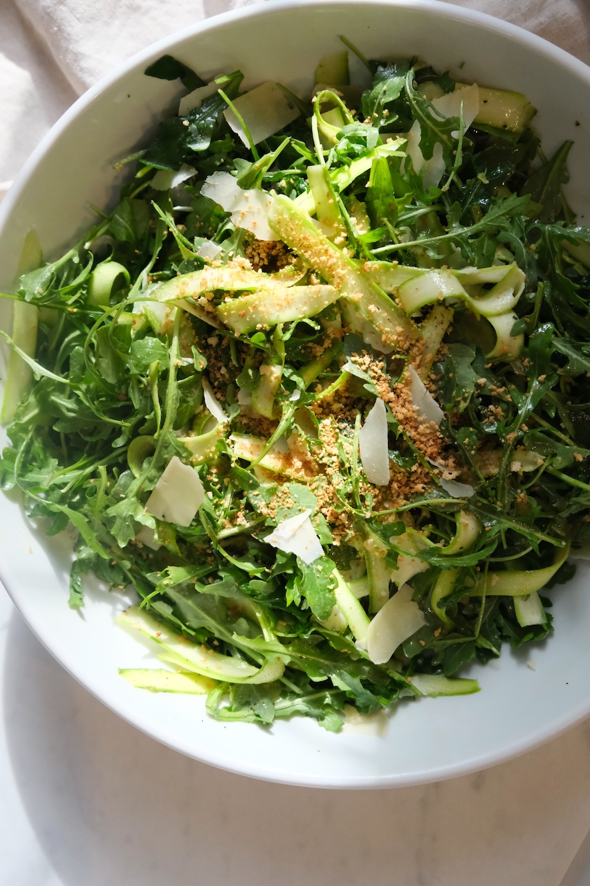 shaved asparagus and arugula salad in a large white bowl