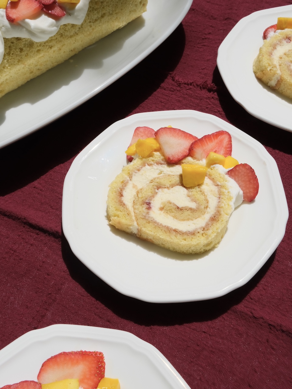 slice of strawberry mango swiss roll cake on a white plate with a red background