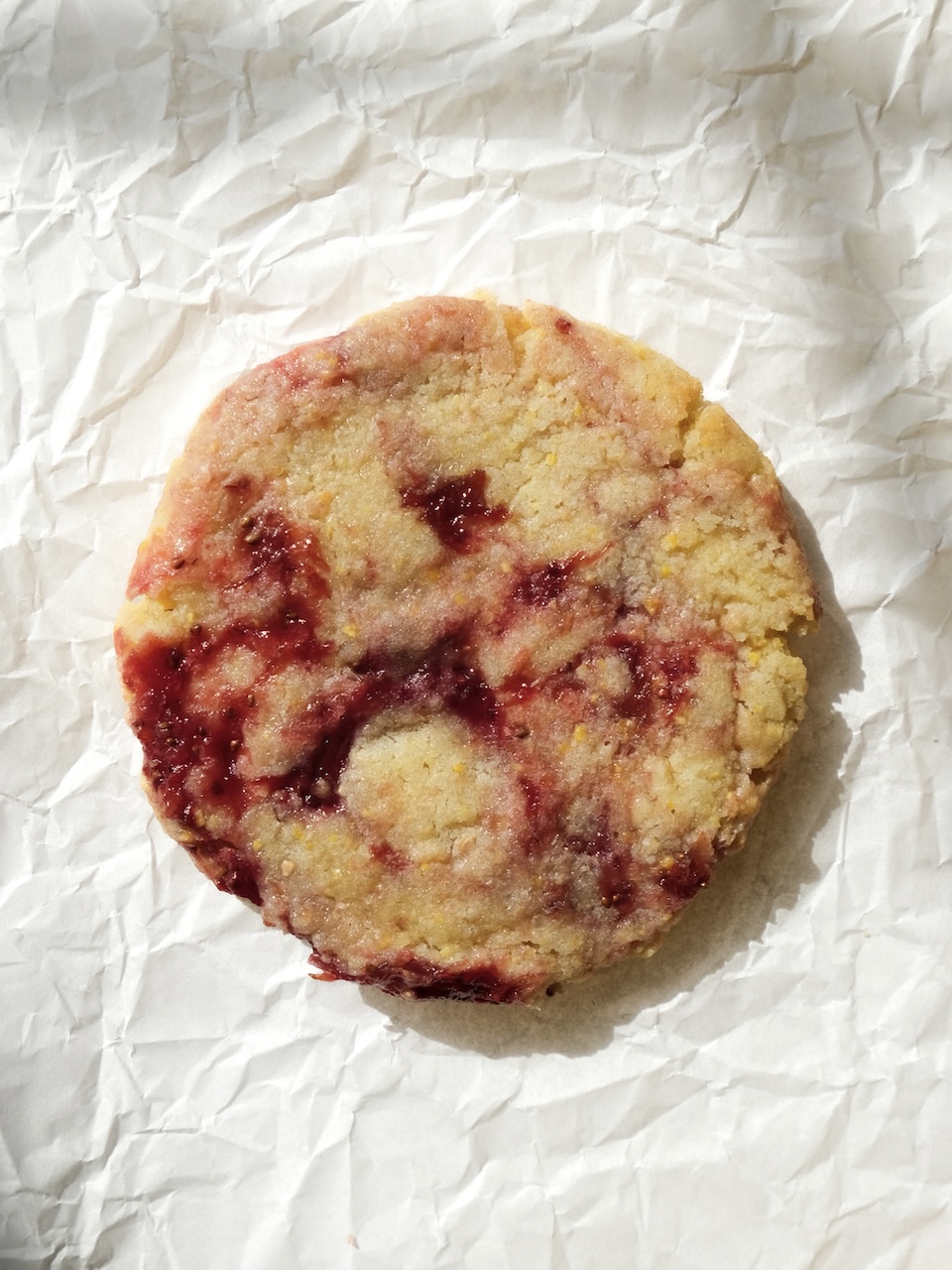 a single strawberry cornmeal cookie laying flat on white parchment