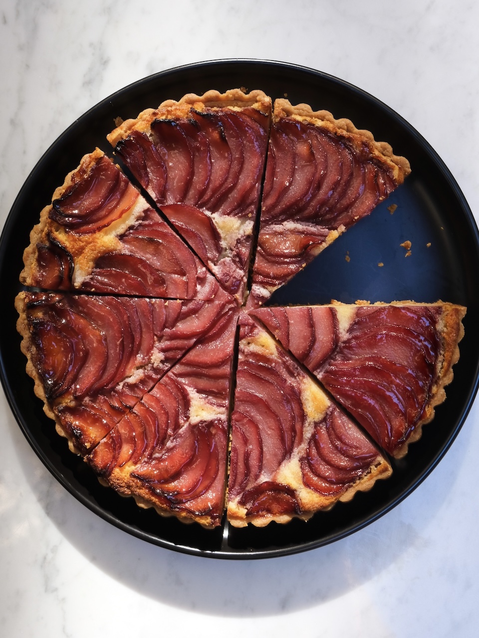 whole almond pear tart, on a black platter, on a white surface
