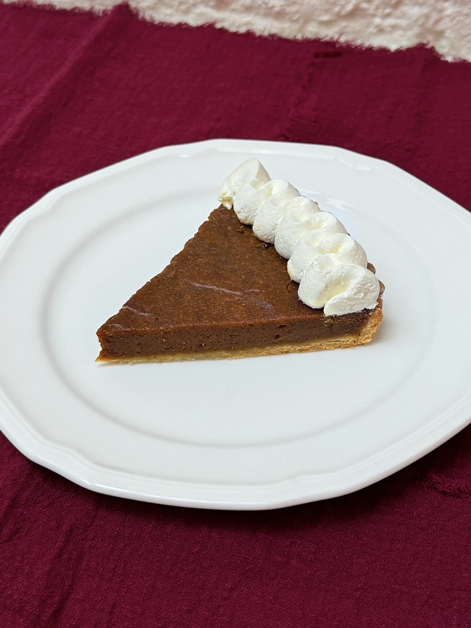slice of pumpkin tart, on a white plate, on a red cloth