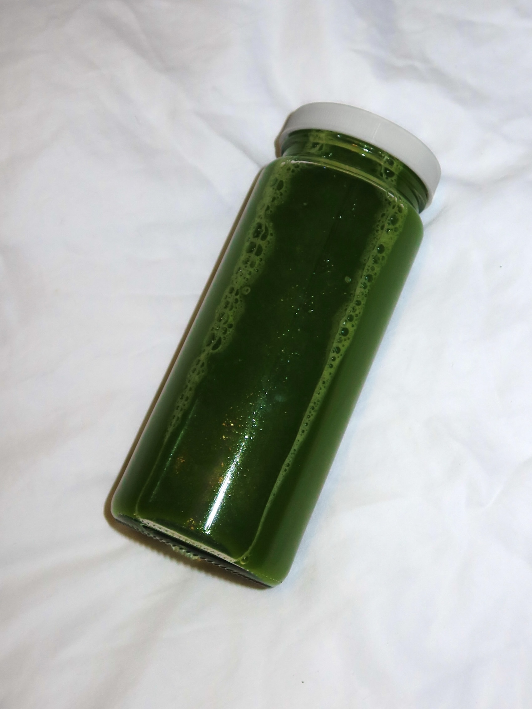 a bottle of green juice laying flat on a white bed
